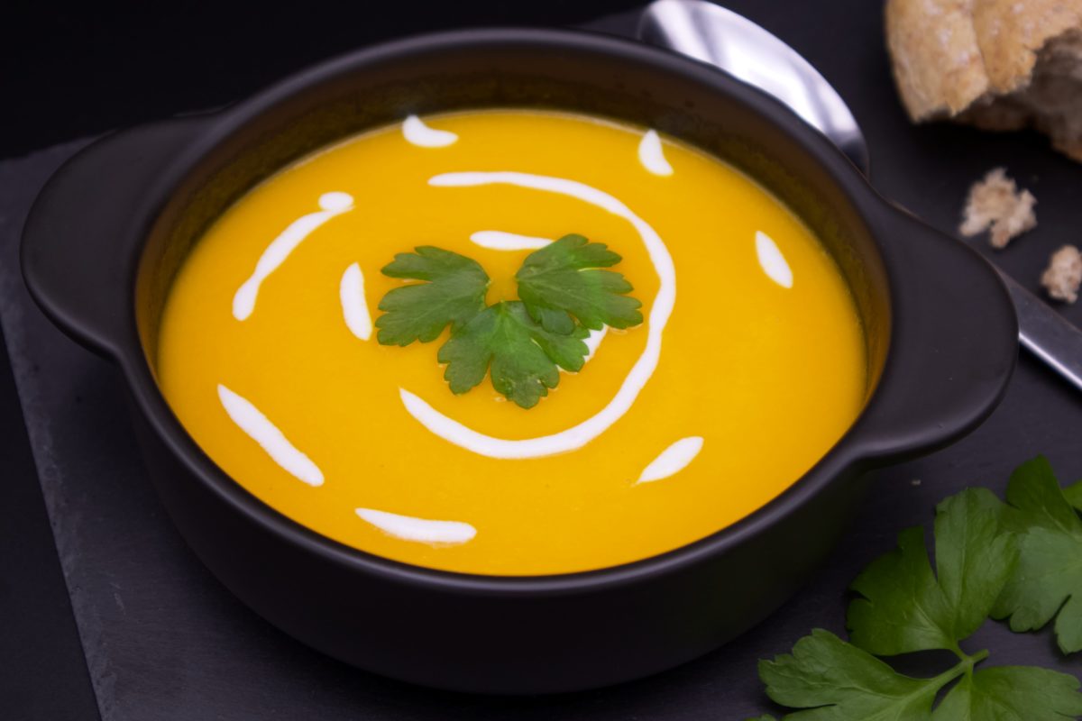 Carrot and Ginger Soup in a bowl garnished with parsley and rustic bread.